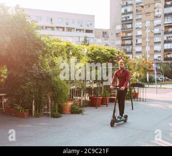 In voller Länge von schönen jungen bärtigen kaukasischen Mann mit Sonnenbrille Fahrten auf der Straße e Scooter Stockfoto