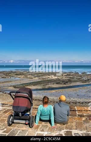 Ein Paar sitzt auf dem Pier mit Blick auf das Meer und eine Austernfarm in Cancale, Bretagne, Frankreich. Stockfoto