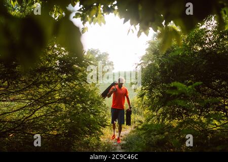Ein sportlicher Fitness-Kaukasianer in einem orangefarbenen T-Shirt geht zum Training im Wald. Outdoor-Sport Stockfoto