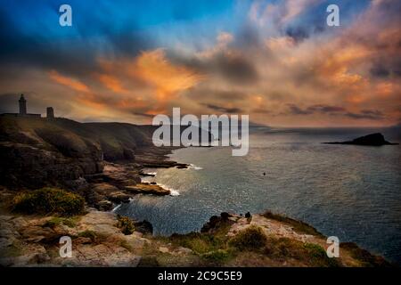 Côte de Granite Rose, Bretagne, Frankreich. Spektakulärer Sonnenuntergang auf der Klippe mit Blick auf das Meer und die Leuchttürme des Cap Fréhel. Rote Wolken am Himmel. Stockfoto