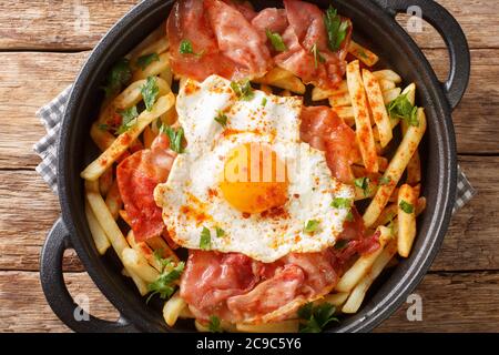 Huevos Rotos Rezept: Spanische zerbrochene Eier mit Kartoffel und Jamone Nahaufnahme in einem Teller auf dem Tisch. Horizontale Draufsicht von oben Stockfoto