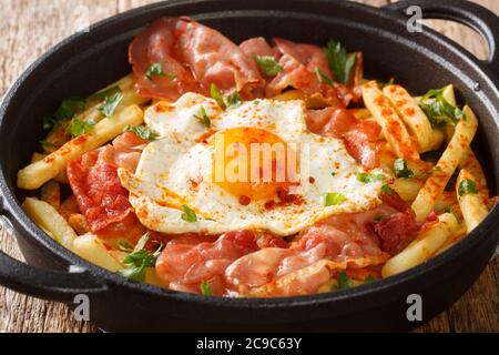 Huevos Rotos Rezept: Spanische zerbrochene Eier mit Kartoffel und Jamone Nahaufnahme in einem Teller auf dem Tisch. Horizontal Stockfoto