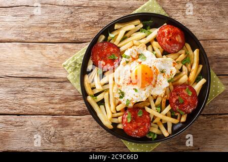 Huevos Rotos mit Bratkartoffeln und Chorizo Nahaufnahme in einem Teller auf dem Tisch. Horizontale Draufsicht von oben Stockfoto