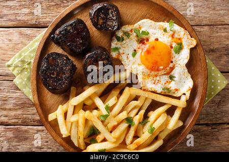 Huevos Rotos Rezept: Spanische zerbrochene Eier mit Kartoffel und Blutwurst close-up in einem Teller auf dem Tisch. Horizontale Draufsicht von oben Stockfoto