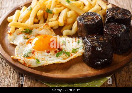 Huevos Rotos Rezept: Spanische zerbrochene Eier mit Kartoffel und Blutwurst close-up in einem Teller auf dem Tisch. Horizontal Stockfoto