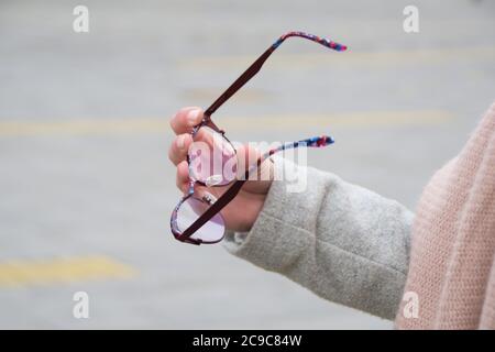 Nahaufnahme der Hand einer Frau, die eine Lesebrille auf einer Straße hält. Negatives Leerzeichen. Platz für Werbung kopieren. Stockfoto