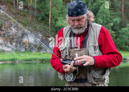 Reifen Fliegenfischen Fischer nimmt Fliegen für Angelrute Ausrüstung. Machen Sie bereit Angeln Stockfoto