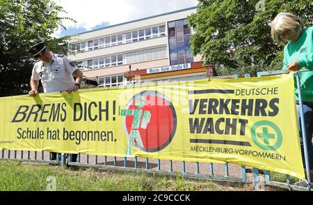 Rostock, Deutschland. Juli 2020. Matthias Bartsch, Präventionsbeauftragter der Rostocker Polizei, und Angelika Stiemer, Verkehrswache, befestigen vor der Grundschule am Mühlenteich ein Transparent mit der Aufschrift "Brems dich! Die Schule hat begonnen." Am 03.08.2020 beginnt wieder der Unterricht für rund 150,000 Schüler in Mecklenburg-Vorpommern. Quelle: Bernd Wüstneck/dpa-Zentralbild/ZB/dpa/Alamy Live News Stockfoto