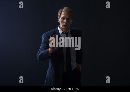 Stoppen Sie es, ein junger Mann Geschäftsmann in einem Anzug und Krawatte macht eine Geste des Protests. Portrait im Studio auf dunklem Hintergrund. Stockfoto