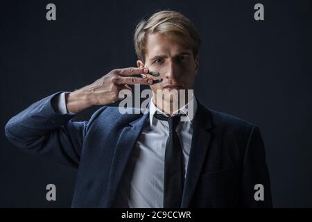 Geschäftsmann zieht zwei Streifen auf seine Wangen, Kriegsfarbe. Wettbewerb im Geschäft, Konzept. Ein junger Mann in Anzug und Krawatte macht Kriegsfarbe auf sein Gesicht. Stockfoto