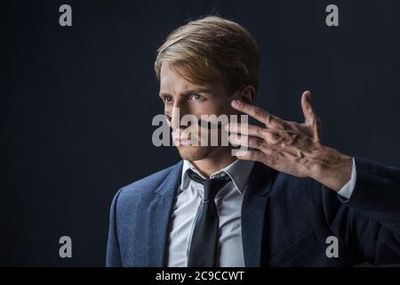 Geschäftsmann zieht zwei Streifen auf seine Wangen, Kriegsfarbe. Wettbewerb im Geschäft, Konzept. Ein junger Mann in Anzug und Krawatte macht Kriegsfarbe auf sein Gesicht. Stockfoto