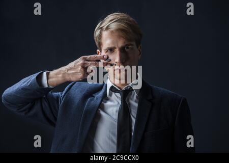 Geschäftsmann zieht zwei Streifen auf seine Wangen, Kriegsfarbe. Wettbewerb im Geschäft, Konzept. Ein junger Mann in Anzug und Krawatte macht Kriegsfarbe auf sein Gesicht. Stockfoto