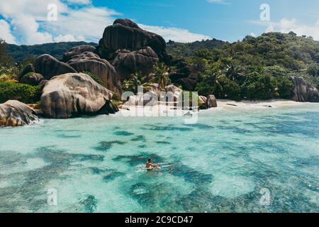 Insel 'La digue' auf den Seychellen. Silberner Strand mit Granitstein und Dschungel. Mann, der Urlaub am Strand genießt und Spaß mit dem Kajak hat. Antenne V Stockfoto