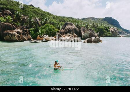 Insel 'La digue' auf den Seychellen. Silberner Strand mit Granitstein und Dschungel. Mann, der Urlaub am Strand genießt und Spaß mit dem Kajak hat. Antenne V Stockfoto