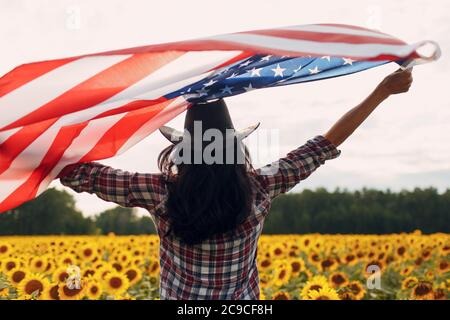 Junge Frau mit Flagge der Vereinigten Staaten von Amerika im Sonnenblumenfeld. 4. Juli Independence Day USA Konzept. Stockfoto