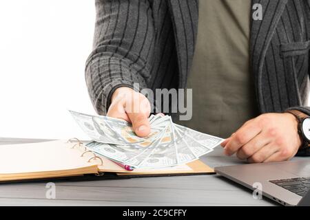 Mann in Anzug hält in einem Arm Pack von hundert Dollar Rechnungen, während Sie am Tisch sitzen Stockfoto