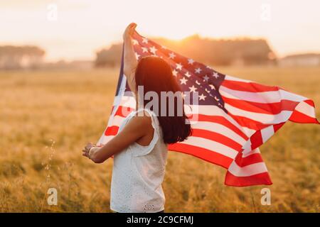 Frau Bäuerin auf dem landwirtschaftlichen Feld mit amerikanischer Flagge auf Sonnenuntergang Stockfoto
