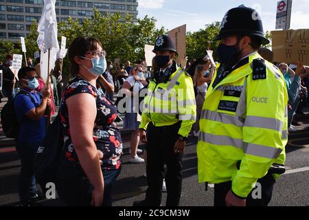 Maskierte Polizeibeamte versuchen, Aktivisten davon zu überzeugen, aus der Westminster Bridge Road auszuziehen, während Mitarbeiter des National Health Service (NHS) gegen ihren Ausschluss von einer kürzlich angekündigten Gehaltserhöhung im öffentlichen Sektor protestieren. Demonstration vor dem St. Thomas' Hospital in London.rund 900,000 Beschäftigte des öffentlichen Sektors in ganz Großbritannien werden in diesem Jahr als Dank des Finanzministeriums für ihre Bemühungen während der Coronavirus-Pandemie eine überhöhte Lohnerhöhung erhalten. Die Gehaltserhöhung ist jedoch ausschließlich für Krankenschwestern und andere Mitarbeiter vor der Haustür aufgrund eines drei-Jahres-Lohnabschlusses, den sie 2018 ausgehandelt haben, was sie zu m führte Stockfoto