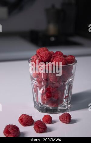 Transparentes Glas mit Himbeeren auf weißem Tisch in grauer Küche. Hochwertige Fotos Stockfoto