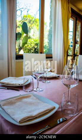 Tischset für eine Zeremonie in einem italienischen Restaurant. Feiern für eine Hochzeit. Korb mit Champagner. Blumenschmuck. Rosa Tischdecke. Luxus, Ele Stockfoto