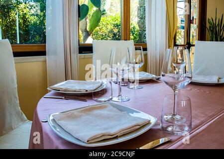 Tischset für eine Zeremonie in einem italienischen Restaurant. Feiern für eine Hochzeit. Korb mit Champagner. Blumenschmuck. Rosa Tischdecke. Luxus, Ele Stockfoto