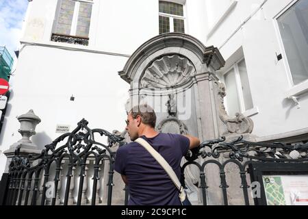 Brüssel Belgien - ein Mann besucht die berühmte Manneken Pis Wasserfontäne Statue eines kleinen Jungen, der einen kleinen Jungen nimmt Stockfoto