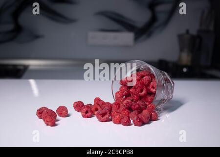 Transparentes Glas mit Himbeeren auf weißem Tisch in grauer Küche. Hochwertige Fotos Stockfoto