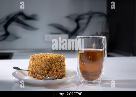 tasse Tee in einem Doppel-Botoom Glas und Stück Kuchen auf weißem Tisch in der grauen Küche. Hochwertige Fotos Stockfoto