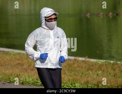 An einem Sommermorgen während der Pandemie läuft eine junge Dame mit einer OP-Maske und Gummihandschuhen. In Kissena Park, Flushing, New York City. Stockfoto