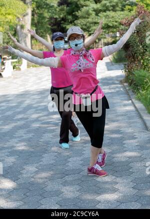 Eine Gruppe von chinesisch-amerikanischen Frauen, die Masken tragen und Distanzen beobachten, üben modernen chinesischen Tanz. Bei einem Outdoor-Kurs in Flushing, Queens, NYC Stockfoto