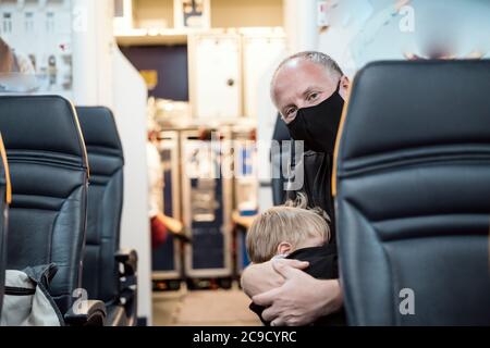 Mann in der Maske hält seinen kleinen schlafenden Sohn im Flugzeug Stockfoto