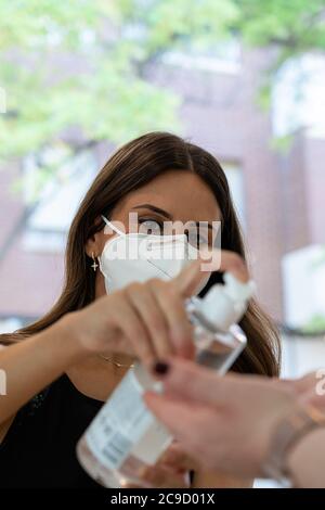 Junger Shop-Assistent durch eine Gesichtsmaske Abgabe hydroalkoholisches Gel an Kunden für die Hygiene gegen Bakterien auf den Händen geschützt. Vermeidung von in Stockfoto