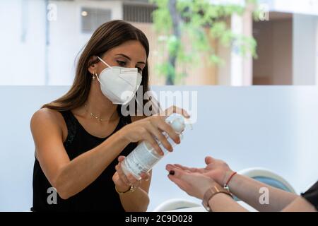 Junger Shop-Assistent durch eine Gesichtsmaske Abgabe hydroalkoholisches Gel an Kunden für die Hygiene gegen Bakterien auf den Händen geschützt. Vermeidung von in Stockfoto