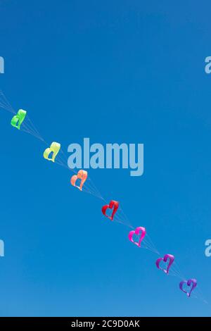 Eine Reihe von Regenbogenfarben Herz geformten Drachen fliegen in den blauen Himmel. Hintergrund oder Hintergrundbild. Vertikale Aufnahme. Stockfoto