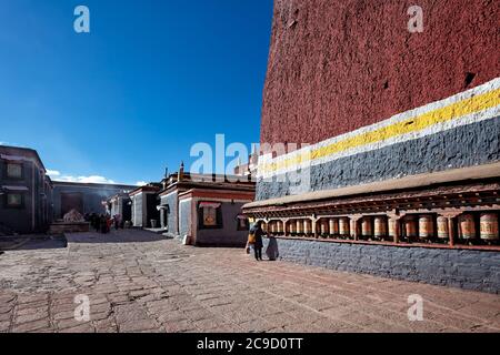 Ein Pilger geht entlang einer Reihe von Gebetsrädern im Sakya Kloster, Tibet. Stockfoto