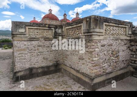 Steinmetzplatten in den Ruinen der Zapotec-Stadt Mitla. Im Hintergrund sind die Kuppeln der Kirche San Pablo zu sehen. Mitla, Oaxaca, Mexiko. Stockfoto