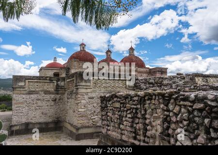 Steinmetzplatten in den Ruinen der Zapotec-Stadt Mitla. Im Hintergrund sind die Kuppeln der Kirche San Pablo zu sehen. Mitla, Oaxaca, Mexiko. Stockfoto