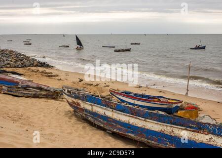 Verwitterte Daus am Sandstrand von Maputo, Mosambik, wobei andere Boote den kleinen Fischerhafen am frühen Morgen verlassen Stockfoto