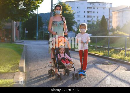 Kinder mit Mutter gehen mit Gesichtsmasken für COVID-19 auf der Straße. Selbstisolierung und soziale Distanzierung. Stockfoto