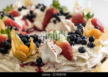 Köstlicher pavlova-Kuchenkranz aus französischer Baiser und Schlagsahne, verziert mit Erdbeere, Blaubeeren und Physalis Stockfoto