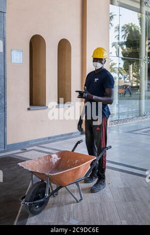 Bauarbeiter mit gelben Schutzmützen und Gesichtsmasken arbeiten an der Renovierung eines Hotels in Costa Adeje nach dem Covid 19 l Stockfoto