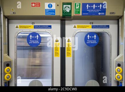 London über dem Boden geschlossene Zugtür mit fahrenden Zug durch Fenster gesehen. Soziale Abstandsschilder klebten am Fenster. Stockfoto