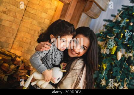 Weihnachten Familienportrait von glücklich lächelnde Mutter umarmt kleine Tochter in der Nähe von weihnachtsbaum. Winterurlaub Weihnachten und Neujahr Konzept Stockfoto