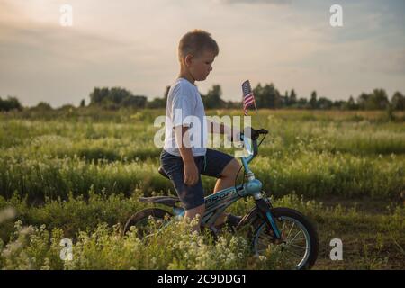 Junge auf dem Fahrrad in einem 4. Juli auf dem Wind auf dem grünen Feld. Patriotische Familie feiert Verfassung und Vatertag. Stockfoto