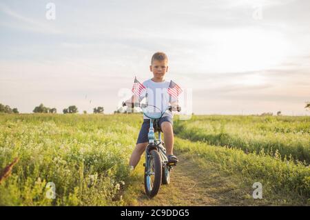 Junge auf dem Fahrrad in einem 4. Juli auf dem Wind auf dem grünen Feld. Patriotische Familie feiert Verfassung und Vatertag. Stockfoto