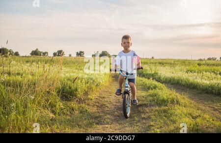 Junge auf dem Fahrrad in einem 4. Juli auf dem Wind auf dem grünen Feld. Patriotische Familie feiert Verfassung und Vatertag. Stockfoto