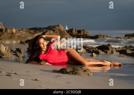 Junge Latina Frau in rotem Badeanzug posiert bei Sonnenuntergang Stunden Am Strand Stockfoto