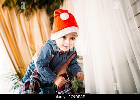 Weihnachten Familienportrait von glücklich lächelnd kleinen Jungen in roten santa Hut in den Händen des Vaters. Winterurlaub Weihnachten und Neujahr Konzept Stockfoto