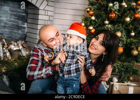 Weihnachten Familienportrait von jungen glücklich lächelnden Eltern spielen mit kleinen Kind in roten weihnachtsmütze in der Nähe des weihnachtsbaumes. Winterurlaub Weihnachten und Neu Stockfoto