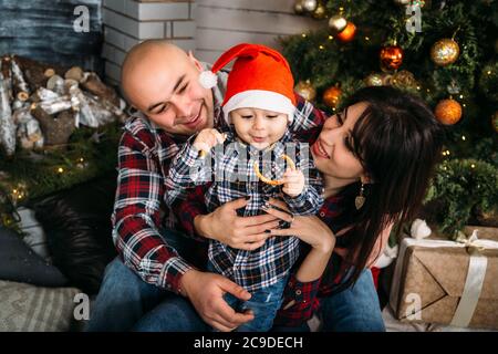 Weihnachten Familienportrait von jungen glücklich lächelnden Eltern spielen mit kleinen Kind in roten weihnachtsmütze in der Nähe des weihnachtsbaumes. Winterurlaub Weihnachten und Neu Stockfoto